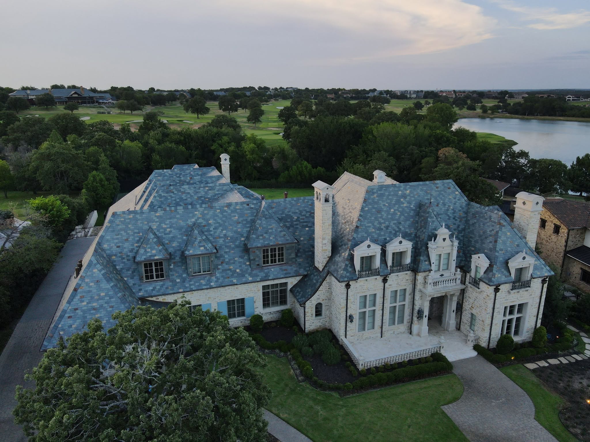 Aerial view of a large white stone house with a new blue-grey slate roof, with a lake and a golf course behind it