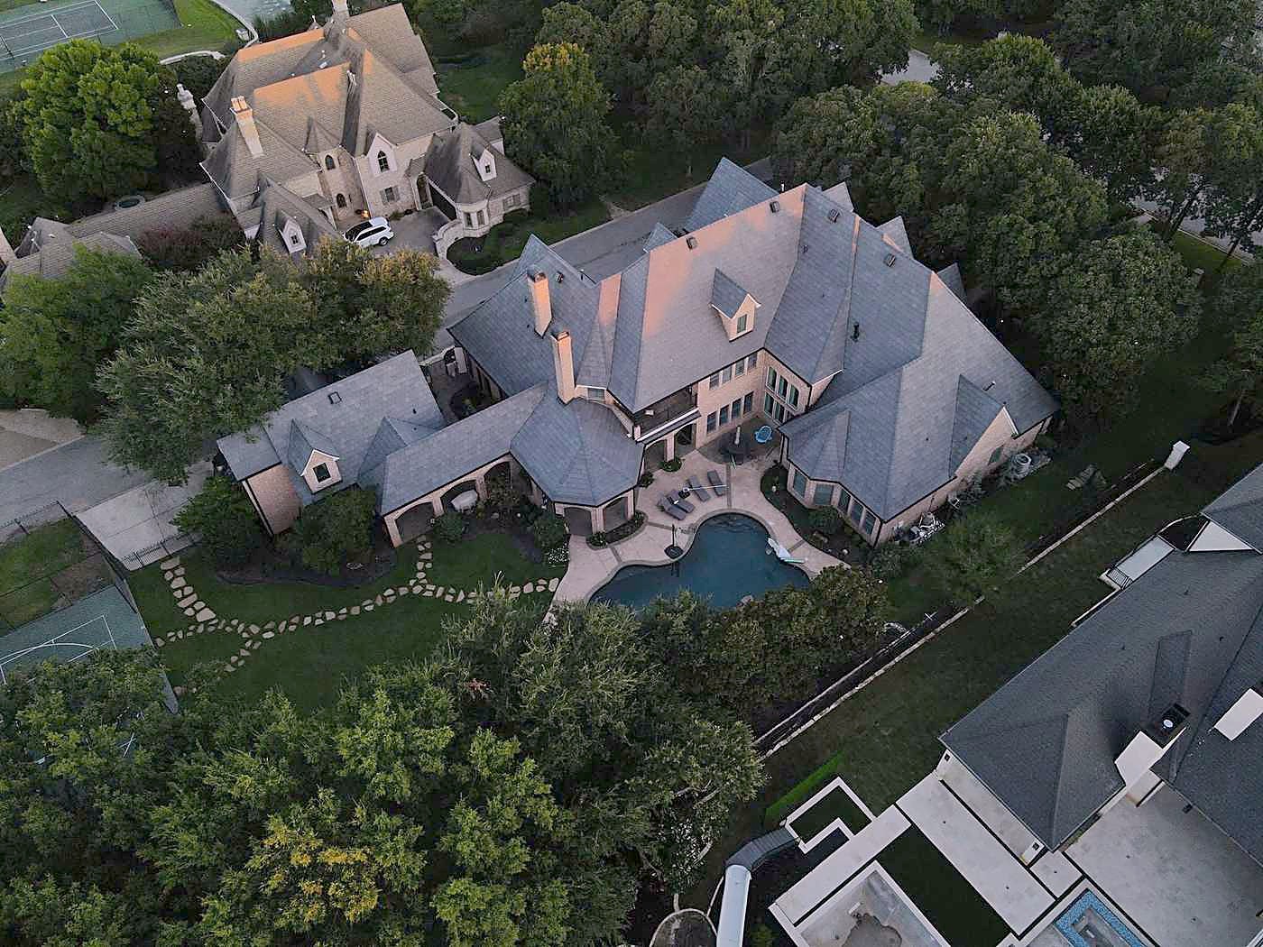 A large grey-roofed house and pool among trees, from the air