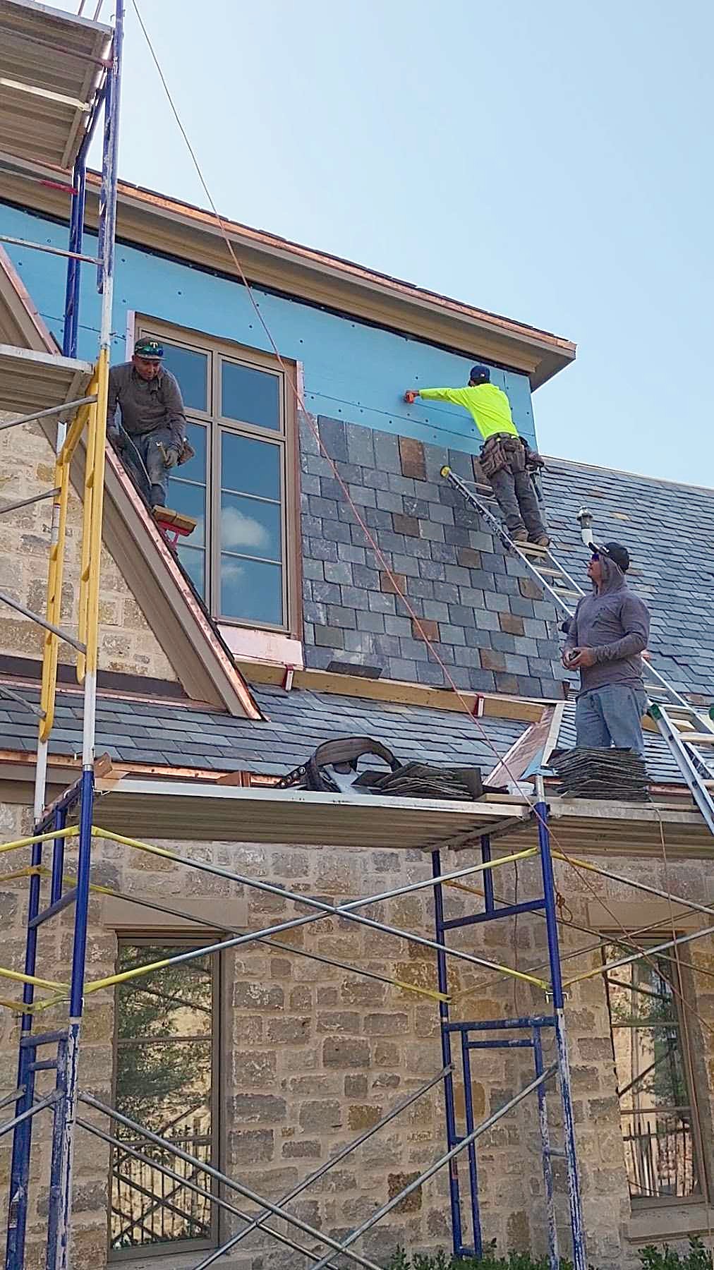 A crew laying slate on a stone house from scaffolding