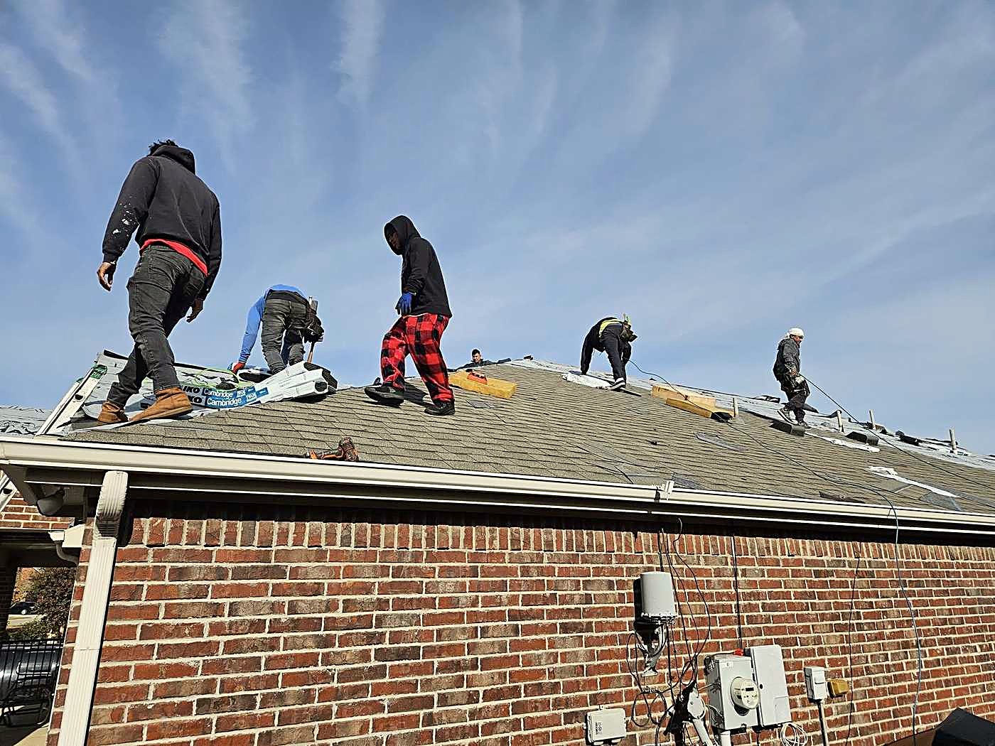 A roofing crew stripping an old roof on a brick house
