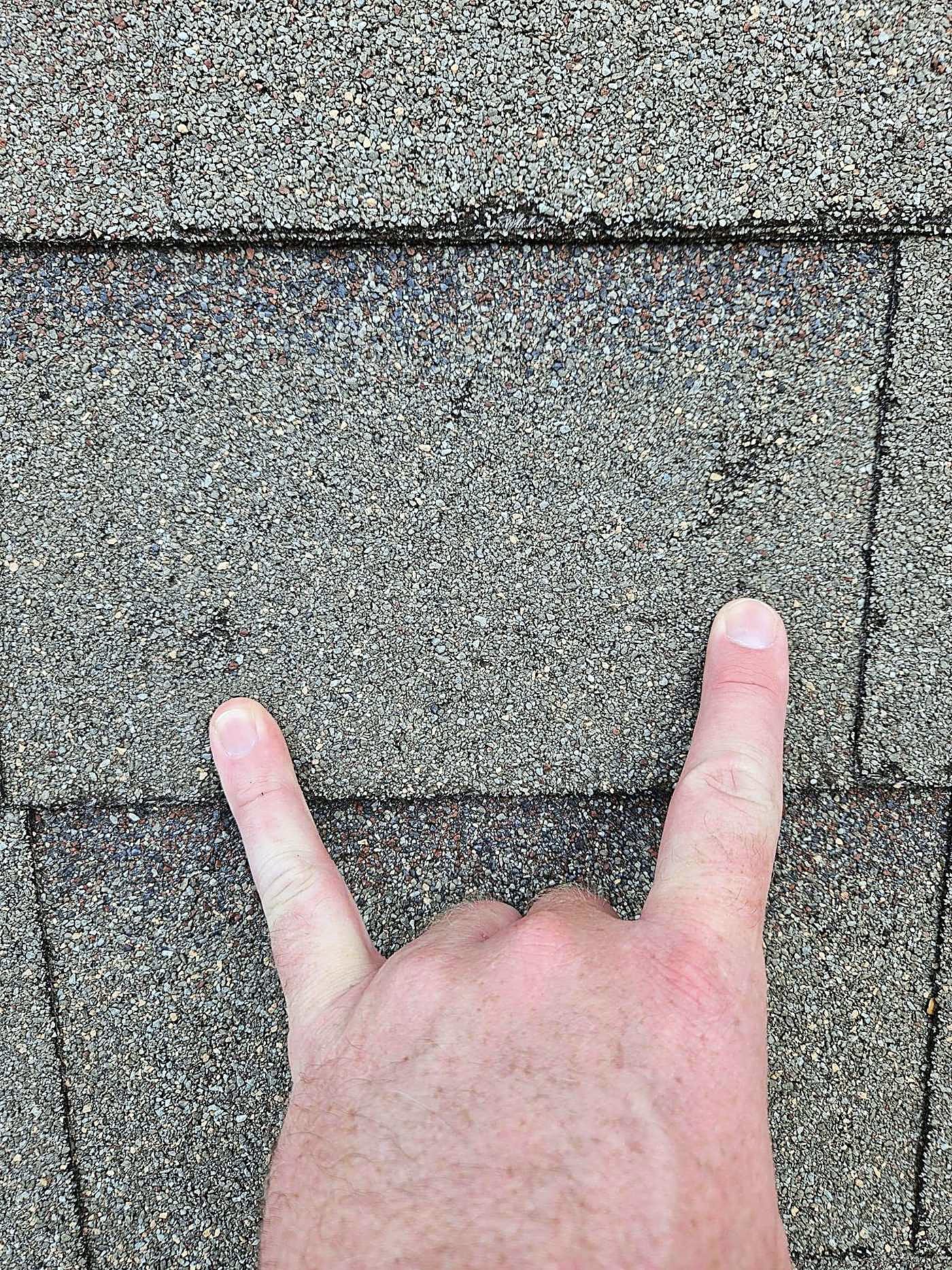 Two fingers pointing at hail hits on an asphalt shingle
