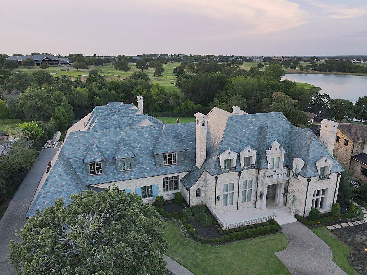 A slate roof on a large stone house by a lake, seen from the air