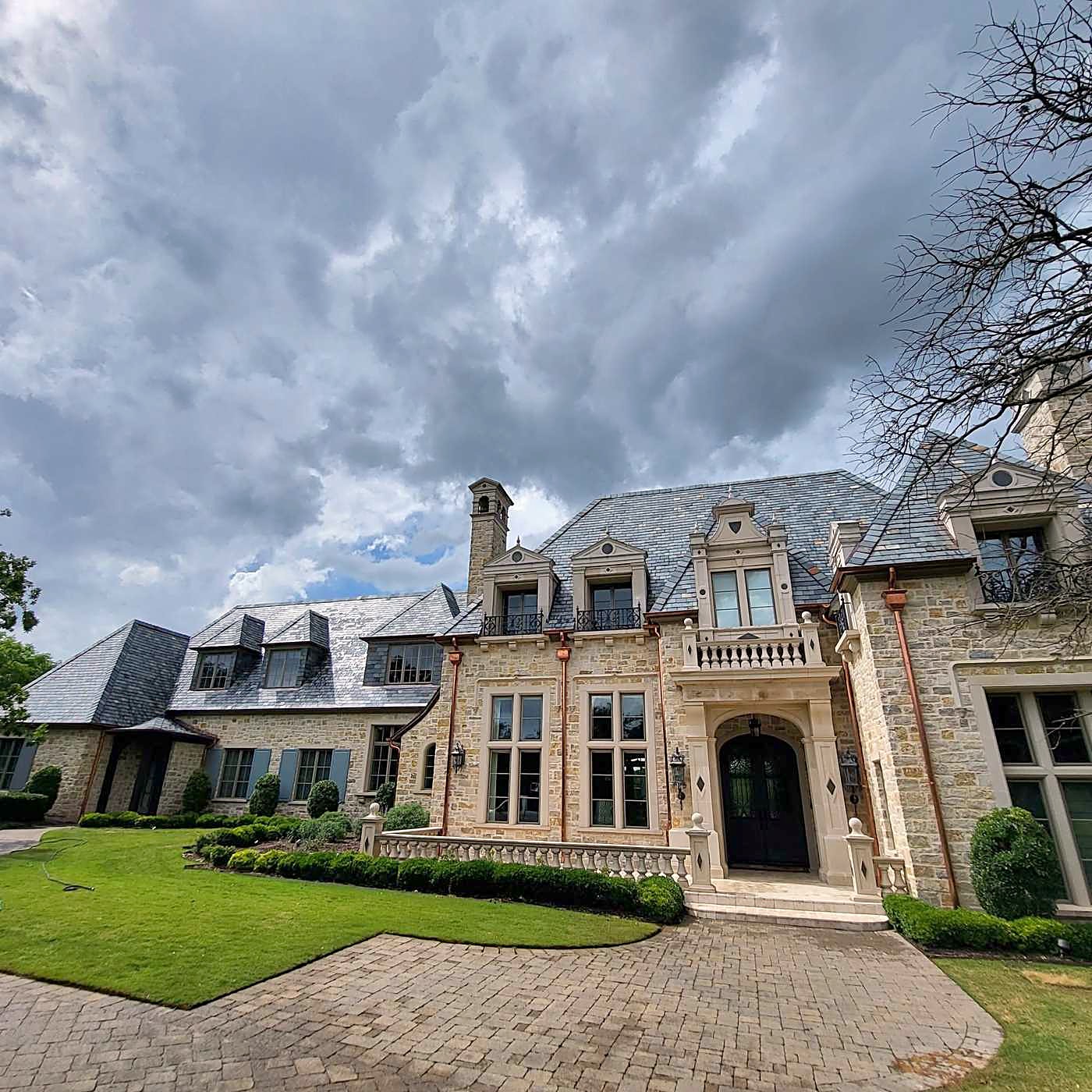 A slate roof on a large stone house under a stormy sky